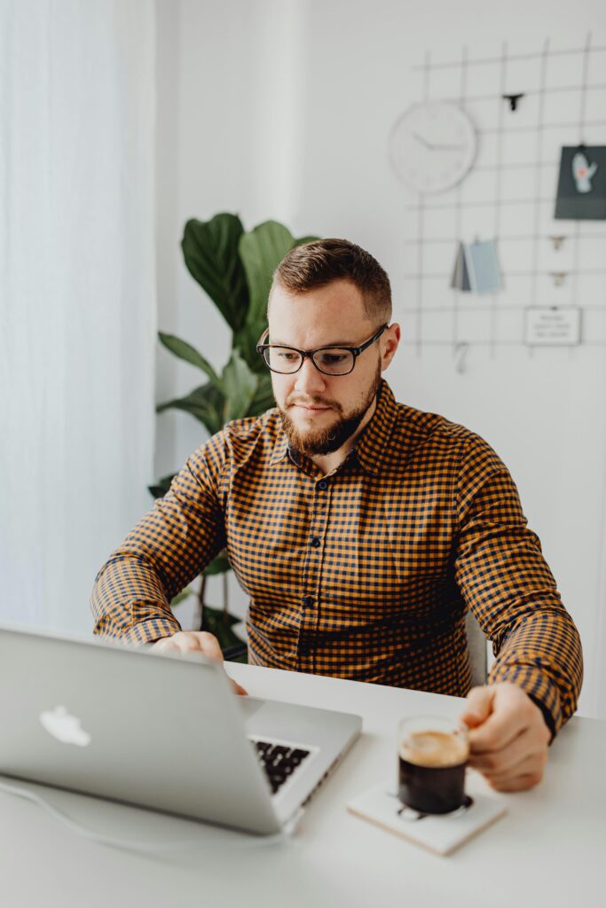 mężczyzna siedzący przy biurku z laptopem i filiżanką kawy, spokojnie przeglądający dokumenty