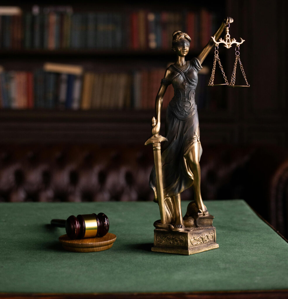 Figura Temidy, symbol sprawiedliwości, stojąca na biurku w otoczeniu książek prawniczych – symbol prawa, spokoju i wsparcia w trudnych sprawach sądowych.